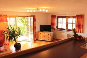 A room with a wooden floor, a television, a dresser, a window with curtains, and a potted plant. - Quiet holiday apartment with lake view (Eggelsberg)