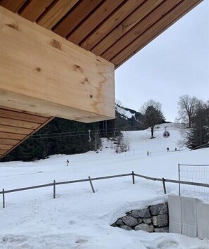 Eine Holzhütte vor einer verschneiten Landschaft mit einer Seilbahn im Hintergrund.