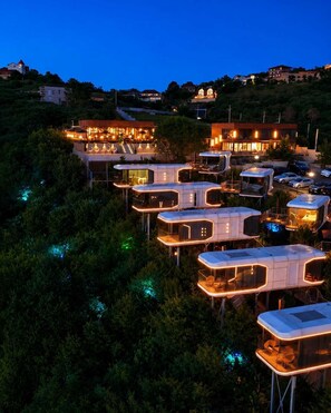Una serie de cabañas modernas y elevadas, con paredes de vidrio, rodeadas de árboles y un paisaje montañoso de fondo.