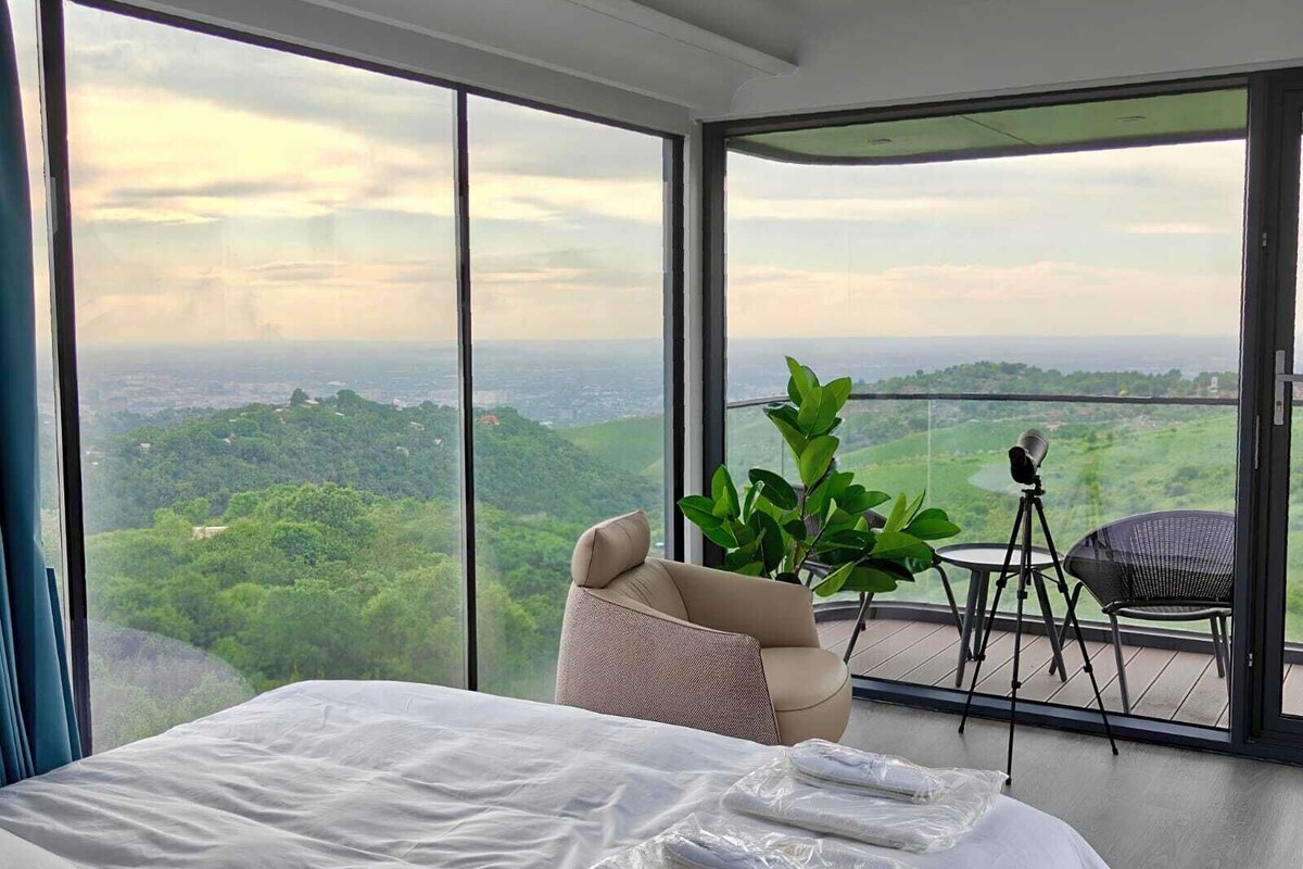 Un dormitorio con una cama grande, vistas a la ciudad y un balcón con una silla y un trípode.