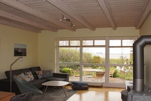 Ein Wohnzimmer mit Sofa, einem kleinen Tisch, einem Kamin und einem großen Fenster mit Blick auf Grünflächen.