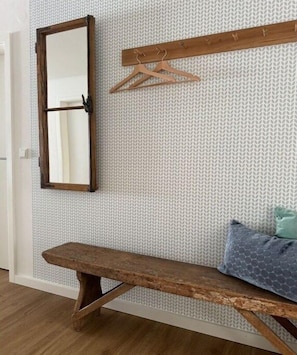 Eine Holzbank, ein Spiegel und ein Kleiderständer aus Holz an einer strukturierten Wand.