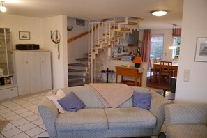 Ein Wohnzimmer mit einer Couch, einer Treppe, einer Küchenzeile und einem Esstisch.