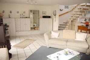 Ein Wohnzimmer mit einer Couch, einem Couchtisch, einem Schrank, einer Treppe und einem Wandbild.