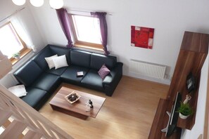 Ein modernes Wohnzimmer mit einem Ecksofa, einem Couchtisch, einem Fernseher und einem Fenster mit Vorhängen.