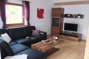Ein Wohnzimmer mit einer schwarzen Couch, einem Holztisch und einem Fernseher auf einem TV-Schrank.