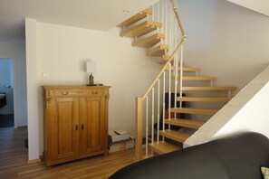 Eine Treppe mit Holzbeschlägen und weißen Geländern, ein Schrank mit Schubladen sowie eine Lampe darauf.