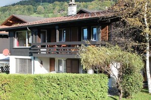 Eine zweistöckige Chalet mit Balkon, Satellitenschüssel und einer gepflegten Hecke davor.