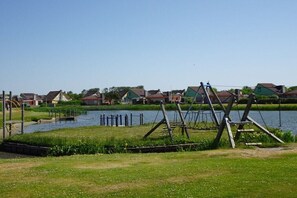 Ein Rasen mit Schaukeln und einem Teich, umgeben von Häusern.