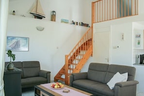 Ein Wohnzimmer mit zwei Sofas, einem Couchtisch mit Obst, einer Treppe und einem Bücherregal.