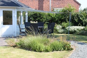 Eine überdachte Terrasse mit Gartenmöbeln, ein Backsteinhaus im Hintergrund und ein Kiesweg.