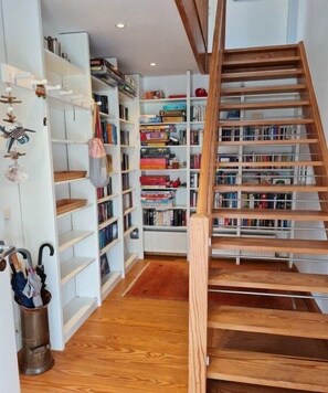Eine Treppe führt zu einem Raum voller Bücher mit Holzböden und weißen Regalen.