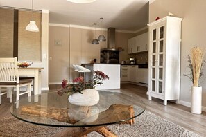 A modern kitchen with white cabinets, a central island, and a dining area with a glass table and chairs. - Apartment Seezeichen in the Baltic Sea resort of Prerow (Ostseebad Prerow)