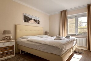 A bedroom with a bed, bedside tables, a window with curtains, and a painting on the wall. - Apartment Seezeichen in the Baltic Sea resort of Prerow (Ostseebad Prerow)