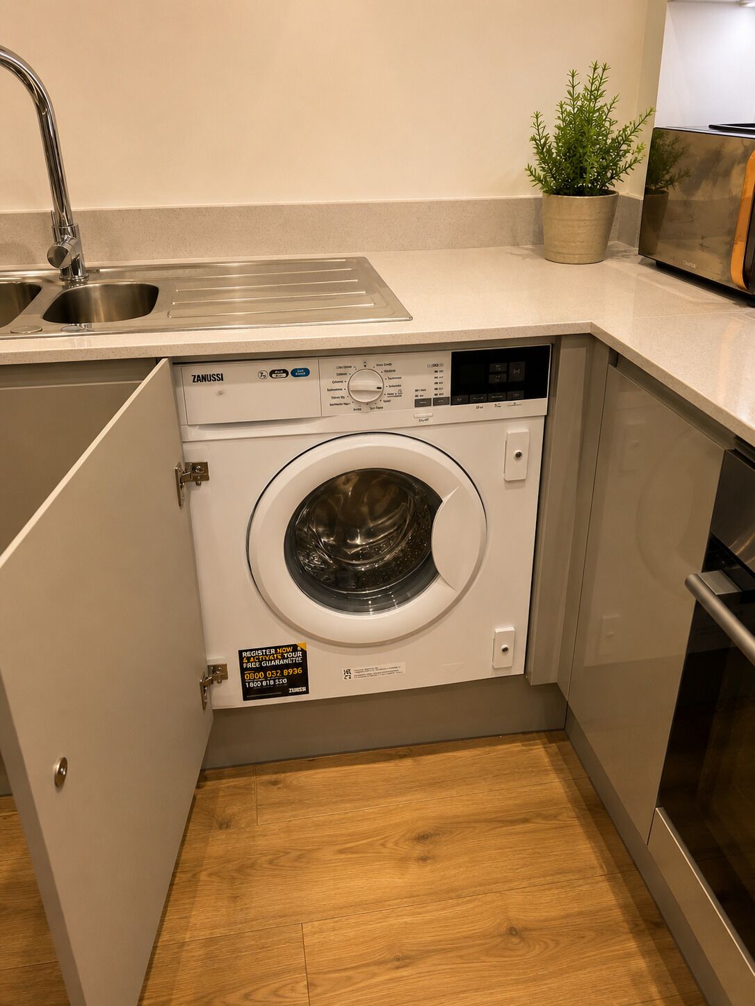 A compact laundry room with a front-loading washing machine, a sink, and a potted plant.