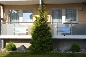 Ein Gebäude mit einem Balkon, einer Fichte und zwei Schildern.