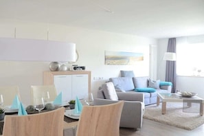 Ein modernes Wohnzimmer mit einer Couch, einem Esstisch und Stühlen. Es gibt ein Sideboard mit einem Radio und Dekoration.
