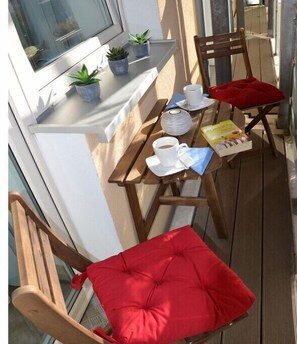 Eine Holzterrasse mit einem Tisch für zwei Personen, Stühle mit roten Kissen und Blumentöpfen auf einem Fensterbrett.
