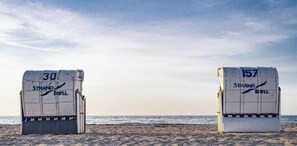 Zwei Strandstühle, beschriftet mit '30 Strand byll' und '157 Strand byll', auf einem sandigen Strand mit dem Meer im Hintergrund.