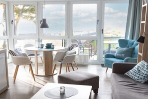 Ein modernes Wohnzimmer mit einem runden Esstisch, zwei Stühlen, einem Sofa und einem blauen Sessel, mit Blick ins Freie.