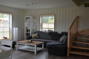 Ein Wohnzimmer mit grauem Sofa, weißem Couchtisch, Bücherregal und Treppe.