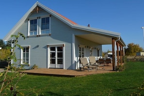 Ein hellblaues Haus mit überdachter Terrasse, großen Fenstern und einem Rasen.