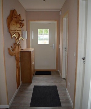 Ein Flur mit einer Holzskulptur, einer Tür mit Fenster und einer Fußmatte im Eingangsbereich.