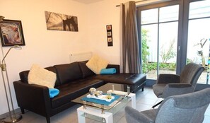 Ein modernes Wohnzimmer mit einer schwarzen Couch, einem Glastisch und grauen Sesseln.