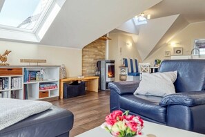 Eine moderne Loftsage mit Dachfenster, Kamin, Ledersofa und Bücherregal.