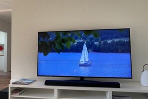 A television mounted on a white stand with a remote control, displaying a sailboat on water. - Holiday apartment with 2 bedrooms (Schluchsee)