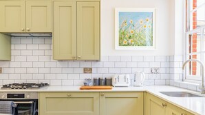A kitchen with light green cabinets, a white tiled backsplash, a toaster, and a coffee maker. - Five-bedroom Victorian townhouse in central Norwich, built for contractor teams. 8 separate beds, 5 bedrooms, 2 off-street parking spaces big enough for vans. 2 great ale pubs across the road. House next door also ours for bigger teams. (Norwich)