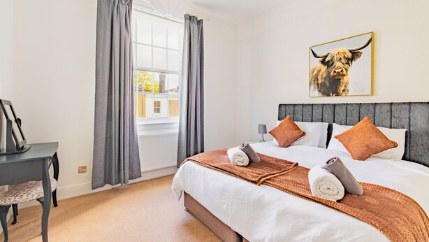 A hotel room with a bed, grey curtains, a window, a painting of a bull, and a desk with a lamp. - Five-bedroom Victorian townhouse in central Norwich, built for contractor teams. 8 separate beds, 5 bedrooms, 2 off-street parking spaces big enough for vans. 2 great ale pubs across the road. House next door also ours for bigger teams. (Norwich)