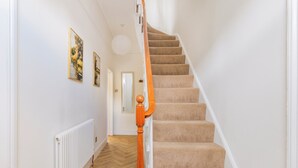 A staircase with carpeted steps and a wooden handrail, leading to a room with a white radiator and wooden flooring. - Five-bedroom Victorian townhouse in central Norwich, built for contractor teams. 8 separate beds, 5 bedrooms, 2 off-street parking spaces big enough for vans. 2 great ale pubs across the road. House next door also ours for bigger teams. (Norwich)