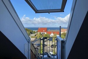 Blick aus einem Fenster mit Metallgeländer auf einen Parkplatz und Gebäude mit roten Dächern, unter blauem Himmel.