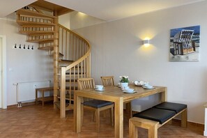Ein Essbereich mit Holztisch, Stühlen, einer Bank, einer Wendeltreppe, einer Wandleuchte und einem Gemälde.