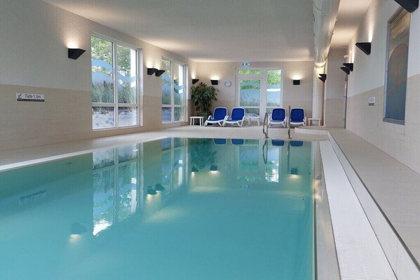 Ein Hallenbad mit Glaswänden, blauen Liegestühlen und einem Schild mit der Angabe der Wassertiefe.