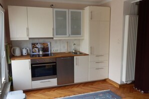 Een compacte keuken met witte kastjes, een vaatwasser, een oven en een spoelbak.