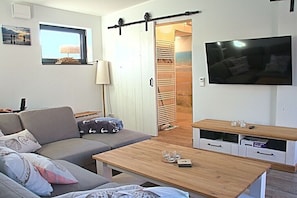A living room with a sofa, coffee table, TV, and a sliding door closet. - Holiday home Lüttes Paradies (Geestland)