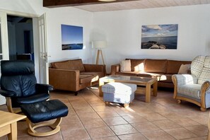 Ein Wohnzimmer mit einem schwarzen Ledersessel, zwei braunen Sofas, einem Holztisch und einem Karo-Sessel.