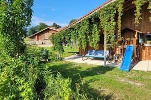 Ein rustikales Holzgebäude mit einer Rutsche, umgeben von Grünflächen und blauem Himmel.