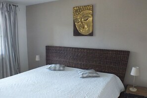 Ein Hotelzimmer mit einem großen Bett, einem Kopfteil, zwei Kissen, einem Wandbild und einem Nachttisch mit Lampe.
