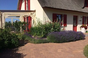 A building with red shutters, a thatched roof, and a garden with various plants. - Holiday home in Zierow with swimming pool (Zierow)