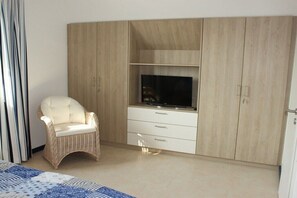 A bedroom with a bed, a television on a cabinet, a wicker chair, and a wardrobe. - Holiday home in Zierow with swimming pool (Zierow)