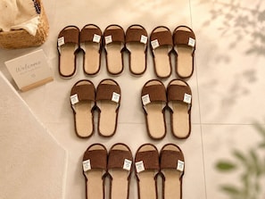 A set of brown slippers with tags, arranged on a tiled floor with a welcome card nearby.