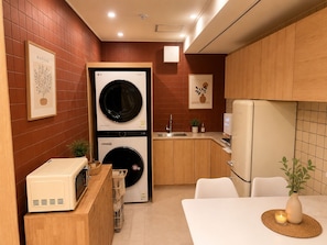 Cocina compacta con lavadora, microondas y refrigerador, armarios de madera y un pequeño comedor.