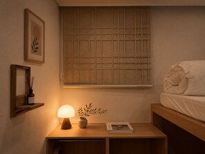 Une chambre à coucher avec une tête de lit en bois, une table de chevet avec une lampe, un tableau encadré, une fenêtre à motifs géométriques et un livre intitulé « KINFOLK ».