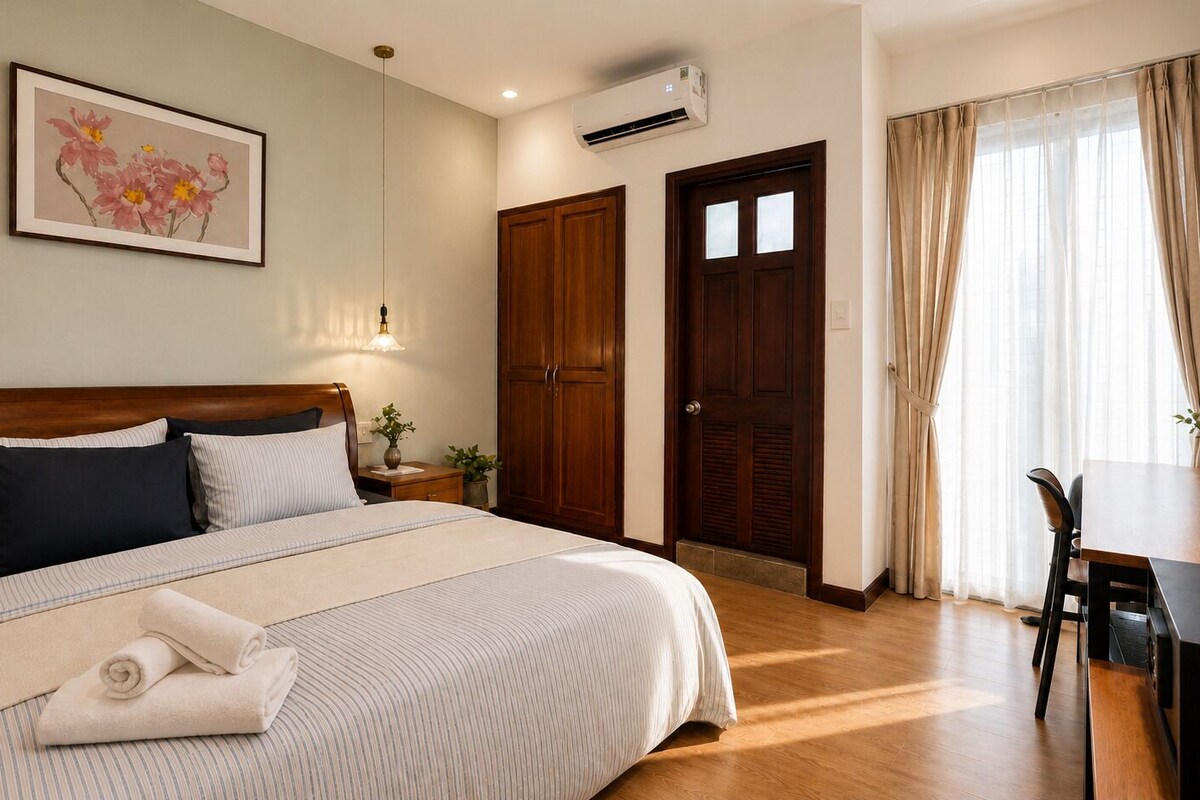A hotel room with a large bed, a desk, a wardrobe, and a painting on the wall.