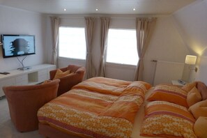 Ein Schlafzimmer mit einem Bett, zwei Stühlen, einem Fernseher und einer Lampe.