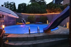 Una piscina con tobogán, zona techada y una silla.