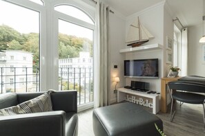 Ein modernes Wohnzimmer mit großem Fenster, einem Flachbildfernseher, einer Couch, einem Couchtisch und einem Essbereich.